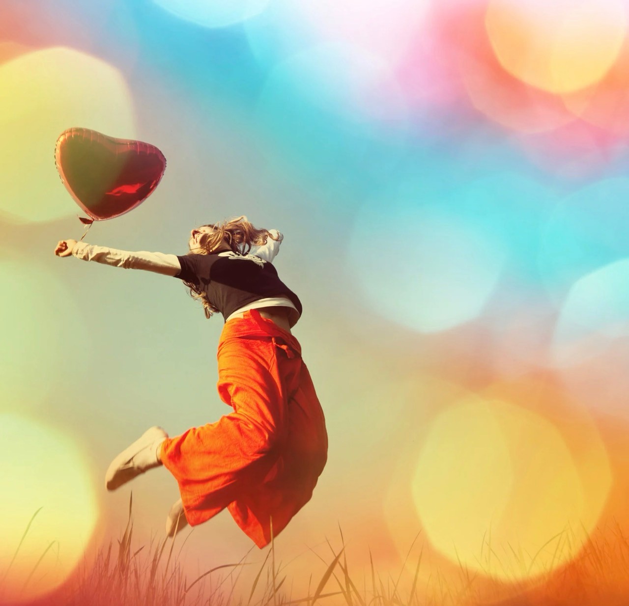 Person jumping with heart balloon in colorful sky